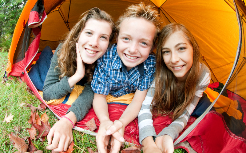 Three anglo kids laying in the doorway of their tent