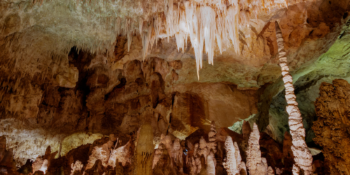 A view inside Carlsbad Caverns, with crystal stalactites dropping from the ceiling, and stalactites emerging from the ground. Colorful.