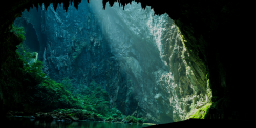 Looking through an opening inside Son Doong Cave, in Vietnam, with a shaft of sunlight creating a green oasis underground.