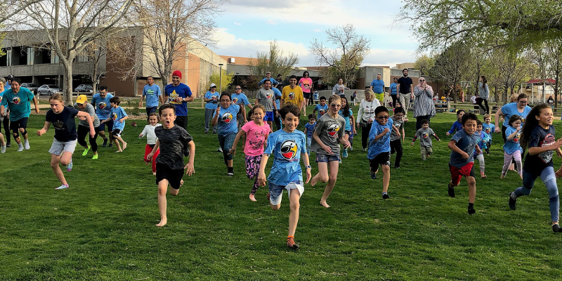 Kids and adults running with Running Medicine on a green lawn (at the campus of the University of New Mexico)<br />
