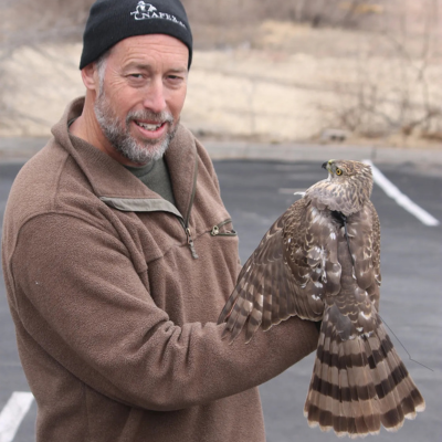 Dr. Brian Millsap wearing a black winter hat and a brown heavy coat and gloves, holding a golden eagle, and facing the camera.